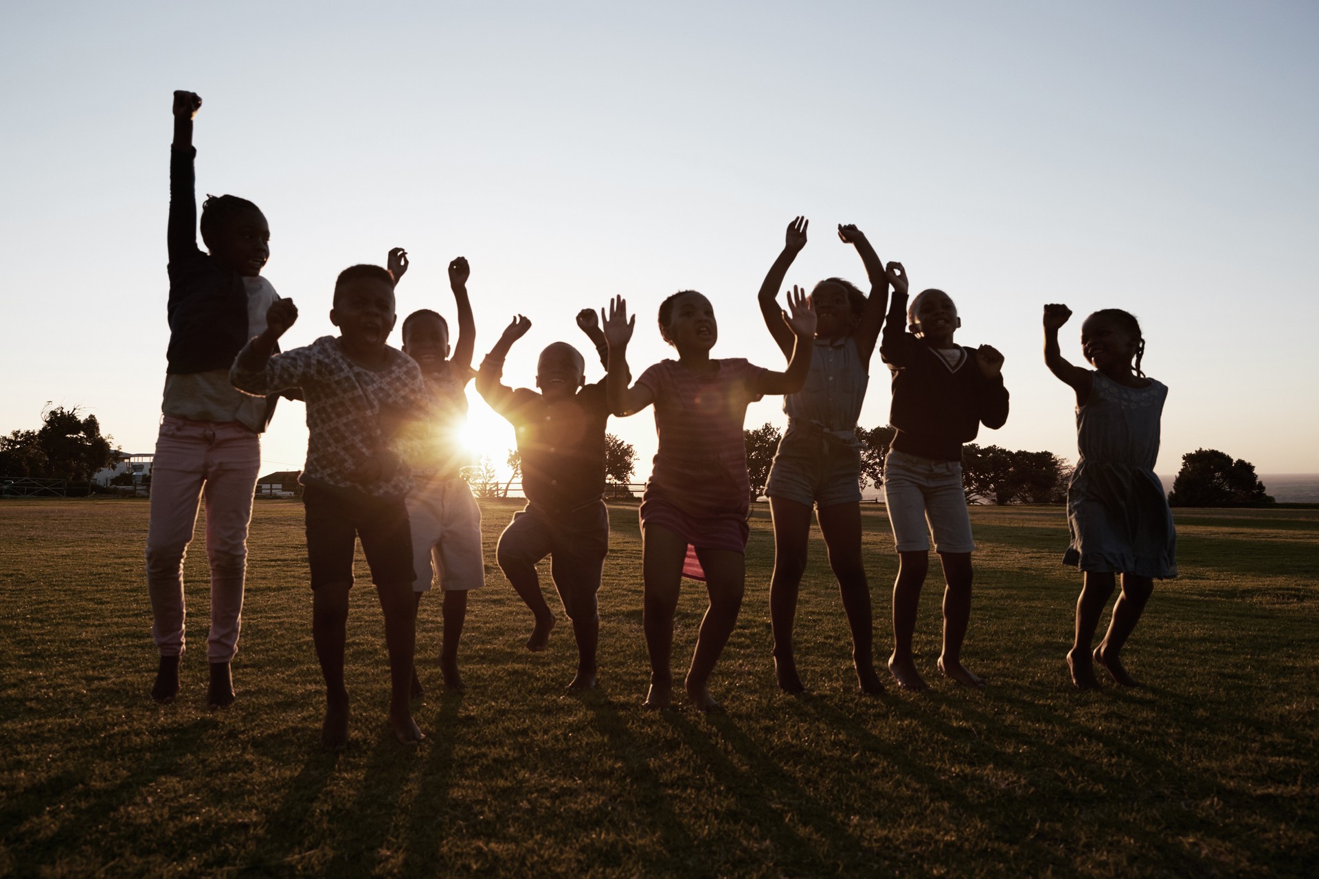 Children jumping in the air with the sun behind them.